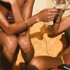 two women in bikinis sitting next to each other holding wine glasses and looking at their cell phones