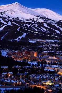 a snowy mountain is in the background with buildings and lights on it at night time