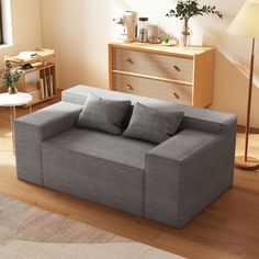 a gray couch sitting on top of a hard wood floor next to a lamp and dresser