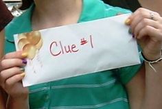 a woman holding up a sign that says clue 1 with donuts on it in front of her