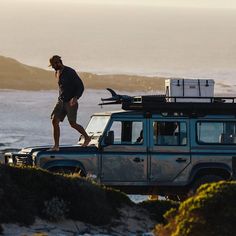 a man walking next to a jeep with a surfboard on top of it's roof