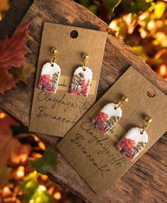 two earrings with flowers on them sitting on top of a wooden table