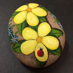 a painted rock with yellow flowers and a ladybug on the center, sitting on a black surface