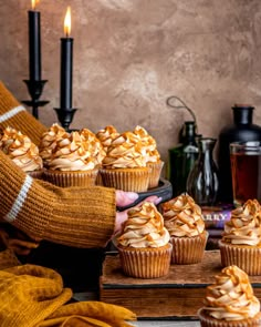 a person holding a plate with cupcakes on it next to candles and bottles