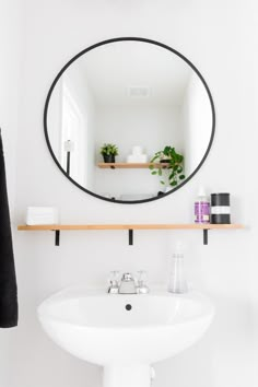 a white sink sitting under a mirror in a bathroom next to a wall mounted shelf