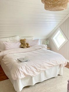 a teddy bear sitting on top of a white bed in a room with slanted ceilings