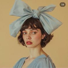 a woman wearing a blue dress with a large bow on her head and hair in the wind