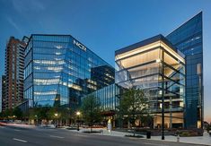 two large glass buildings sitting next to each other on the side of a city street