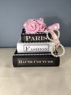 three books stacked on top of each other with a pink rose and pearls attached to them