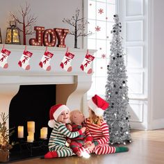 two children sitting on the floor in front of a fireplace with christmas decorations around them