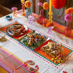 a table topped with lots of food next to vases filled with flowers and candles