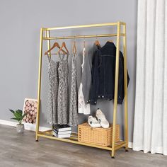 a rack with clothes hanging on it next to a white curtain and wooden flooring