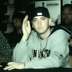 a man sitting at a table with his hands up in the air while wearing a hat