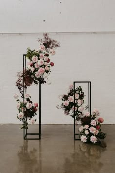 two black stands with flowers on them against a white wall and one has pink roses