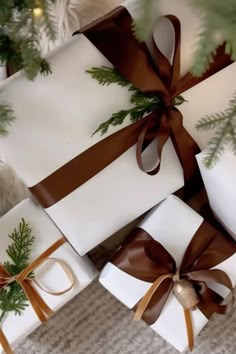 presents wrapped in white paper with brown ribbon and pine cones on them, sitting under a christmas tree