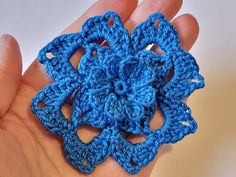 a crocheted blue flower is being held in the palm of someone's hand