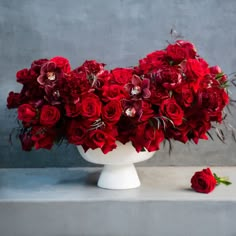 a white vase filled with red flowers on top of a table next to a gray wall