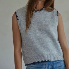 a woman wearing a gray sweater and blue jeans is standing in front of a white wall