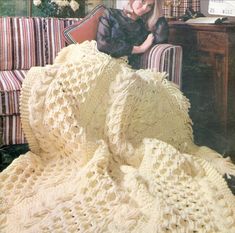 a woman sitting on a couch next to a white crocheted blanket