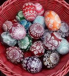 a red basket filled with lots of colorful painted eggs on top of a wooden table