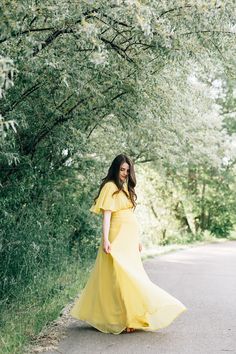 a woman in a yellow dress is walking down the road with her hand on her hip