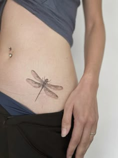 a woman's stomach with a dragonfly tattoo on her lower belly and side