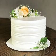 a white cake with flowers and greenery on the top is sitting on a wooden table