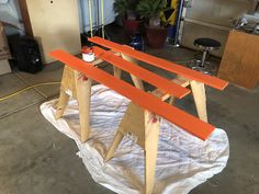 an unfinished wooden bench sitting on top of a white piece of paper next to a potted plant