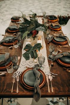 the table is set with plates, silverware and greenery