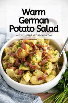 a white bowl filled with potatoes and bacon on top of a wooden table next to greens