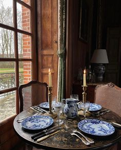 a table set with plates, silverware and candles in front of an open window