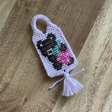 a cross stitch cell phone case with a cat on it's back and tassel