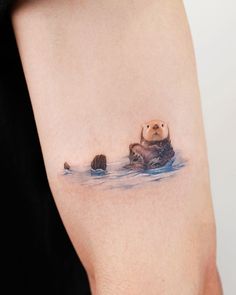 a small otter tattoo on the right side of the arm, with two baby otters swimming in the water