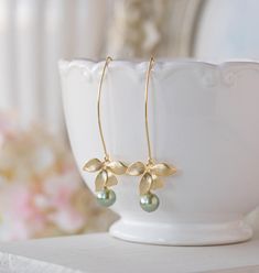 Matte Gold Orchid Flower Sage Green Teardrop Pearls Earrings. Lovely matte gold flowers are hung from gold plated long oval hook ear wires with high quality 8mm Czech round glass pearls dangling beneath. Pearls are in one of my favorite colors, beautiful, elegant and sophisticated sage green :)  Total length of these earrings is approx. 2.5'' (64mm) including the long oval hook ear wires.  Total length: approx. 2.5'' (64mm) Green pearl: 8mm Ear Wires: matte gold plated, High quality plated. Anti Green Pearl Earrings, Pearl Teardrop Earrings, Gold Orchid, Bridal Wedding Earrings, Pearls Earrings, Sage Green Wedding, Costume Jewelry Earrings, Chic Gifts, Green Pearls