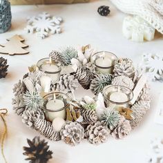 candles are arranged in a wreath with pine cones and snowflakes on the table