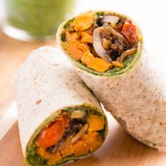 two burritos on a cutting board with a green smoothie in the background