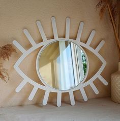 an eye shaped mirror on a shelf next to a vase