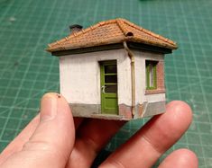 a hand holding up a tiny house made out of paper and clay with a green door