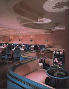 the interior of a fancy restaurant with pink walls and blue chairs, round tables and chandeliers