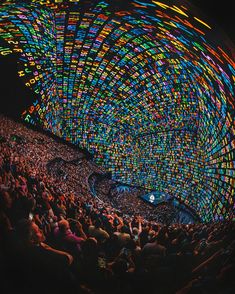 an audience at a concert with colorful lights on the ceiling and people sitting in the seats