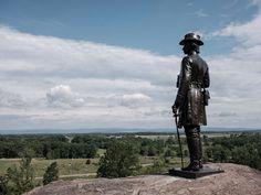 a statue of a man standing on top of a hill with trees in the background