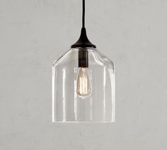 a clear glass light fixture hanging from a black metal ceiling hook on a white wall