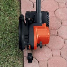 an orange and black lawn mower sitting on top of a brick walkway next to grass