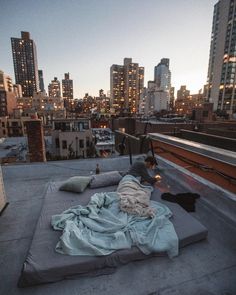 an unmade bed on the roof of a building with city lights in the background