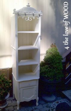 a tall white shelf sitting next to a potted plant in a yard with the words good wood above it