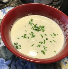 a red bowl filled with white sauce and garnished with parsley in front of an instant pressure cooker