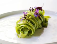 a white plate topped with pasta covered in green sauce and flowers on top of it