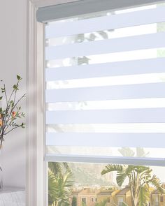 a window with white blinds in front of palm trees and a vase filled with flowers