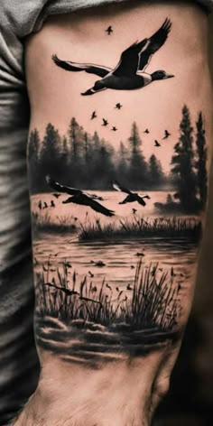 a man's arm with birds flying over the water and trees in the background