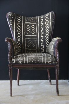 an old chair with black and white designs on it's back, sitting in front of a dark wall